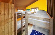 Interior of a safari tent featuring four wooden bunk beds, white bedding, and colorful pillows.