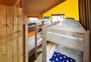 Interieur van een safaritent met vier houten stapelbedden, witte dekens en kleurrijke kussens.