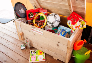 Houten speelgoedkist in een safaritent met gezelschapsspellen, sportmateriaal, een poppenhuisje en strandspeelgoed in beeld.