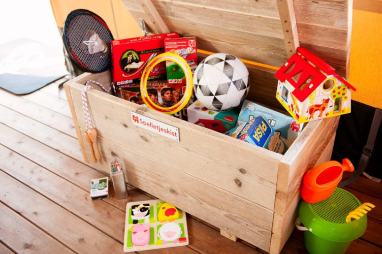 Wooden toy chest in a safari tent with board games, sports equipment, a toy house, and beach toys visible.