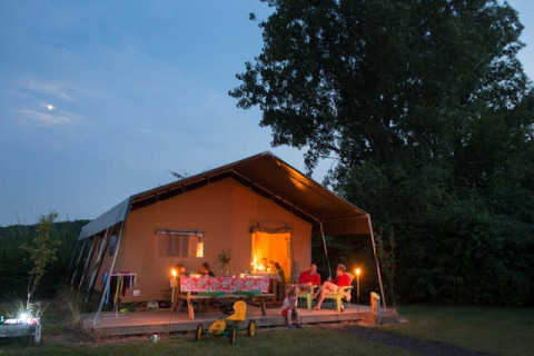 Famille profitant d’une soirée devant une tente safari éclairée, entourée d’arbres, au crépuscule.