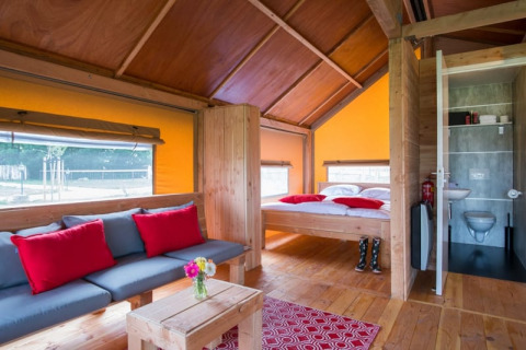 Intérieur de la tente safari Haytent avec meubles en bois, canapé, lit, salle de bain et coussins rouges.