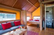 Interior de la tienda safari Haytent con muebles de madera, sofá, cama, baño y cojines rojos.