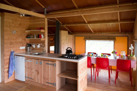 Interior de la tienda safari Haytent con cocina de madera acogedora y comedor con sillas rojas llamativas.