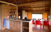 Interior de la tienda safari Haytent con cocina de madera acogedora y comedor con sillas rojas llamativas.