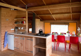 Interior de la tienda safari Haytent con cocina de madera acogedora y comedor con sillas rojas llamativas.