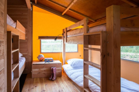 Binnenzicht van de Haytent safaritent met houten stapelbedden, oranje muren en ramen met zicht naar buiten.
