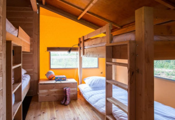 Vista interior de la tienda safari Haytent con literas de madera, paredes coloridas y ventanas al exterior.