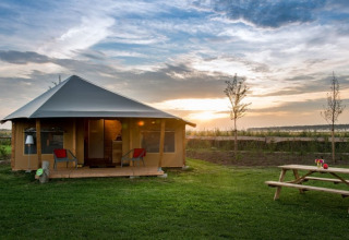 La tienda safari Haytent con porche, césped y mesa de picnic al atardecer en el campo rural.