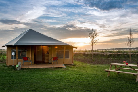 La tenda safari Haytent con veranda, prato verde e tavolo da picnic al tramonto in campagna.