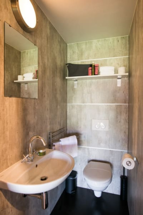 Moderne badkamer in safaritent Haytent met lavabo, spiegel, toilet en plank met verzorgingsproducten.