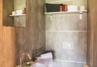 Baño moderno en la tienda safari Haytent, con lavabo, espejo, inodoro y estante para artículos de tocador.