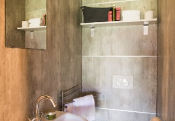 Baño moderno en la tienda safari Haytent, con lavabo, espejo, inodoro y estante para artículos de tocador.