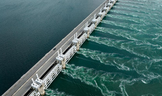 Vista aérea de una presa con carretera y agua fluyendo, situada en un parque de vacaciones con glamping.