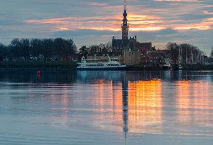 Atardecer sobre Arnemuiden, Zelanda, Países Bajos con torre de iglesia y reflejos en el agua tranquila.