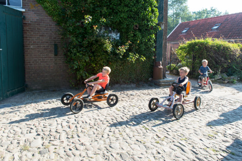 Niños montan karts de pedales en un camino adoquinado en FarmCamps Oranjepolder, parque vacacional en Zeeland.