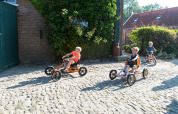 Børn leger på pedalbiler på en brostensbelagt vej ved FarmCamps Oranjepolder, en feriepark i Zeeland.