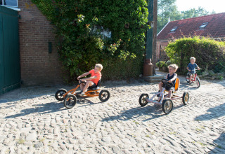 Kinderen racen met trapkarts op een kasseiweg bij FarmCamps Oranjepolder vakantiepark in Zeeland.