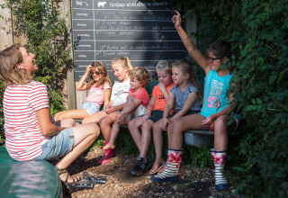 Børn og en voksen sidder og griner sammen udendørs ved FarmCamps Oranjepolder i Zeeland, Holland.