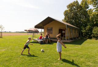 Children play soccer on grass outside a large safari tent at FarmCamps Oranjepolder holiday park, Zeeland.