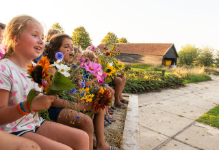 Børn sidder udendørs på en gård i Zeeland, Holland, og holder farverige blomsterbuketter i hænderne.
