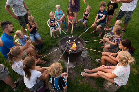 Bambini e adulti arrostiscono marshmallow al fuoco al FarmCamps Oranjepolder, parco vacanze in Zelanda, Paesi Bassi.