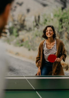 Mujer y hombre juegan al ping-pong en un parque de vacaciones glamping, sonriendo y pasándolo bien al aire libre.