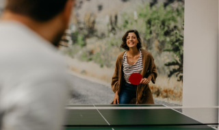 A woman and man playing table tennis at a glamping holiday park, smiling and enjoying their time outdoors.