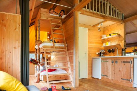 Children playing in a cozy wooden cabin with loft and kitchen at FarmCamps Op de Beemd, North Brabant, Netherlands.