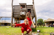 Kinder spielen in roten Overalls vor einem Holzhaus bei FarmCamps Op de Beemd in Nordbrabant, Niederlande.