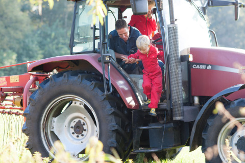 Een kind in rode overall stapt met hulp uit een tractor bij FarmCamps Op de Beemd in Noord-Brabant, Nederland.