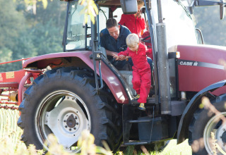 Een kind in rode overall stapt met hulp uit een tractor bij FarmCamps Op de Beemd in Noord-Brabant, Nederland.