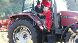 Un niño con mono rojo sale de un tractor ayudado por un adulto en FarmCamps Op de Beemd, Brabante Septentrional, Países Bajos.
