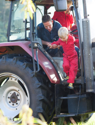 Un niño con mono rojo sale de un tractor ayudado por un adulto en FarmCamps Op de Beemd, Brabante Septentrional, Países Bajos.