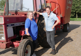 Twee mensen glimlachen bij een rode tractor op FarmCamps Op de Beemd in Noord-Brabant, Nederland.