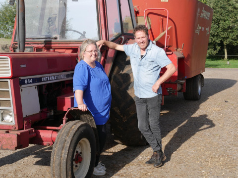 Twee mensen glimlachen bij een rode tractor op FarmCamps Op de Beemd in Noord-Brabant, Nederland.