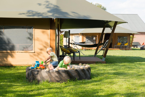 Kinder spielen in einem Traktorreifen-Sandkasten vor Glampingzelten auf FarmCamps Op de Beemd.