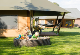 Children playing in a tractor tire sandbox in front of glamping tents at FarmCamps Op de Beemd, Netherlands.