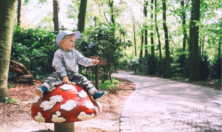 Niño pequeño sentado en una gran seta decorativa en un parque de vacaciones glamping rodeado de bosque.