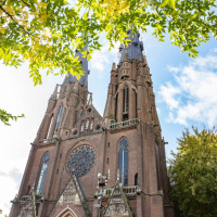 Impresionante catedral gótica con dos torres, vista desde abajo y enmarcada por hojas verdes y cielo azul.