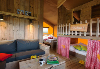 Accogliente interno di una tenda safari Lodgetent con mobili rustici in legno, letti a castello e una calda illuminazione ambientale.