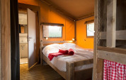 Cozy bedroom inside a Lodgetent safari tent with wood flooring, double bed, and natural light from windows.