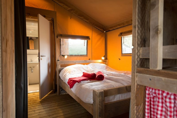 Gemütliches Schlafzimmer in einem Lodgetent-Safarizelt mit Holzfußboden, Doppelbett und natürlichem Licht durch die Fenster.