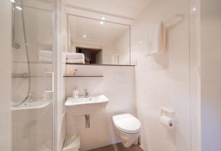 Moderno y compacto cuarto de baño dentro de una tienda de safari Lodgetent, con ducha, lavabo, inodoro y toallas.