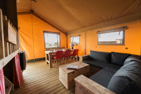 Interiørbillede af et hyggeligt safarilodgetent med træmøbler, en sort sofa og orange lærredsvægge.