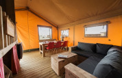 Innenansicht eines gemütlichen Safari-Lodgetents mit Holzmöbeln, einem schwarzen Sofa und orangefarbenen Zeltwänden.