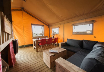 Interiørbillede af et hyggeligt safarilodgetent med træmøbler, en sort sofa og orange lærredsvægge.