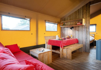 Interno di una tenda safari con mobili in legno, tovaglia rossa, divano accogliente e pareti gialle.