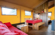 Interior of a safari tent with wooden furniture, red tablecloth, cozy sofa, and warm yellow walls.
