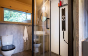 Baño en una tienda safari con ducha moderna, inodoro, lavabo, detalles de madera y ventana grande.